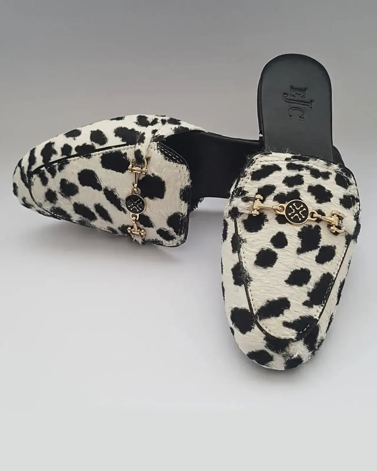 Leopard print slippers with gold chain detail on a gray background