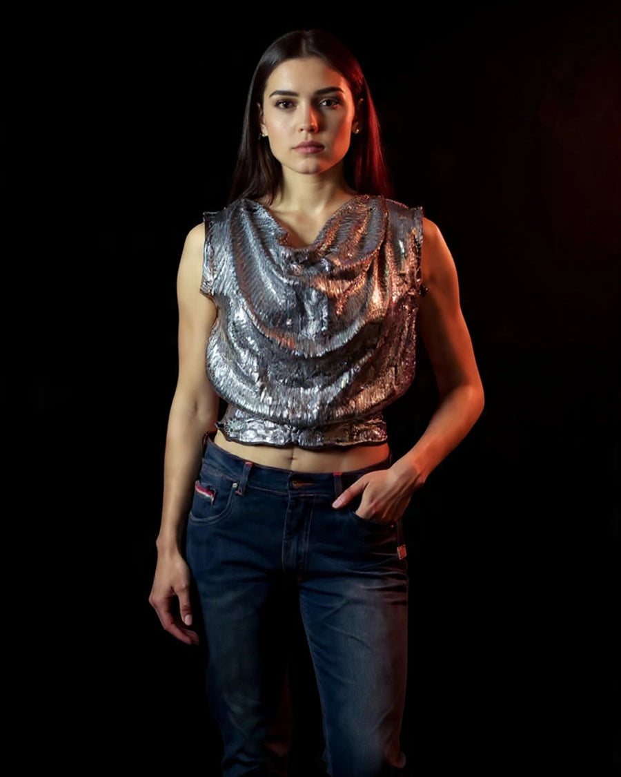 Woman wearing a silver sequin top and blue jeans against a dark background