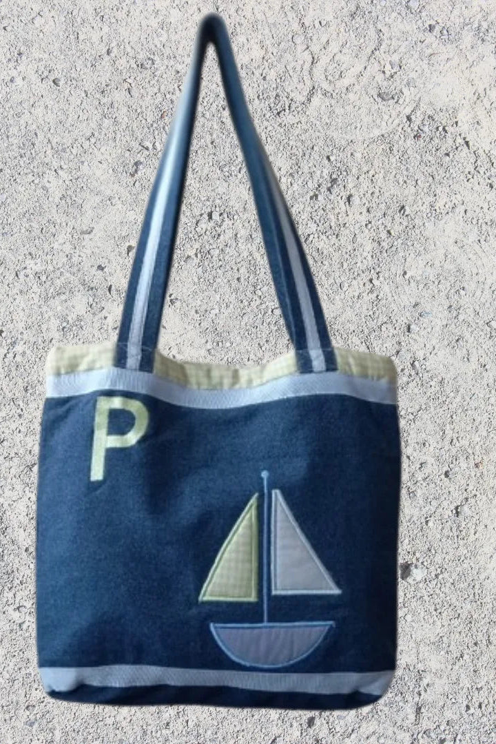 Navy tote bag with sailboat design and letter 'P' on a concrete surface