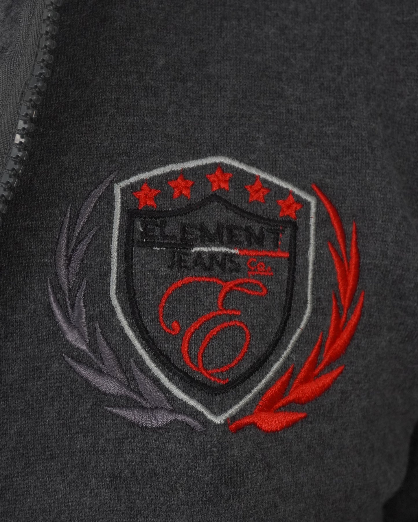 Close-up of a dark gray jacket with an embroidered logo featuring stars and flames.