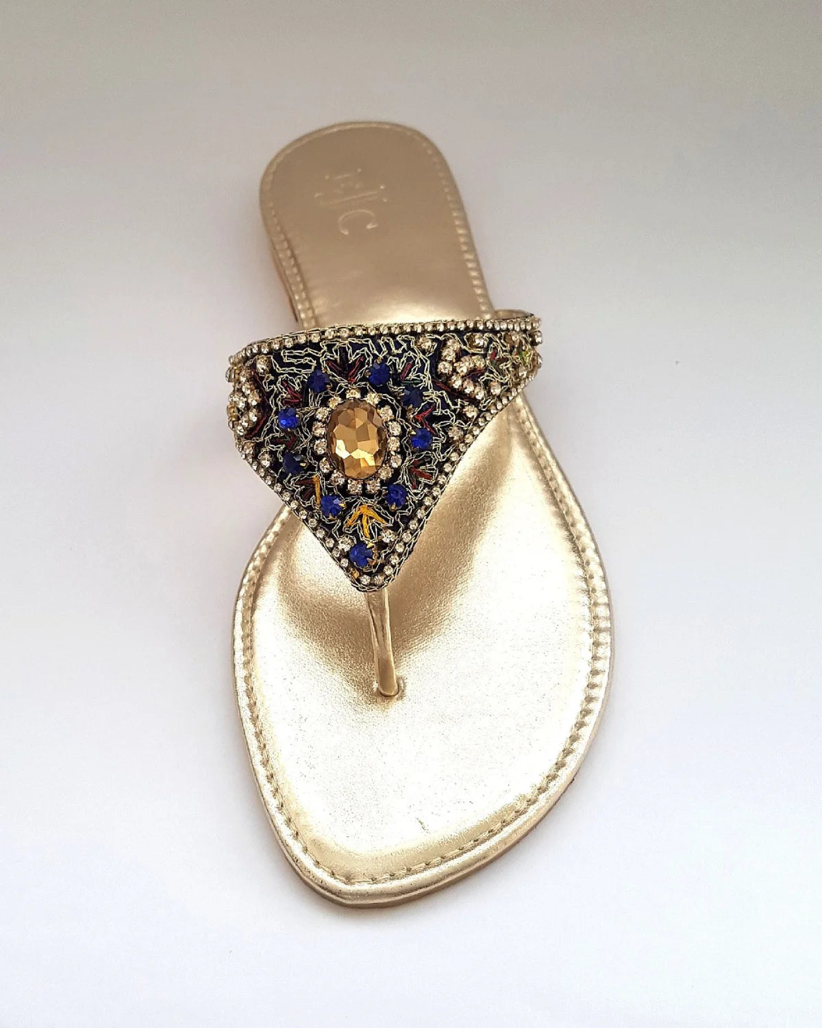 Gold sandal with decorative strap featuring blue and gold stones on a white background