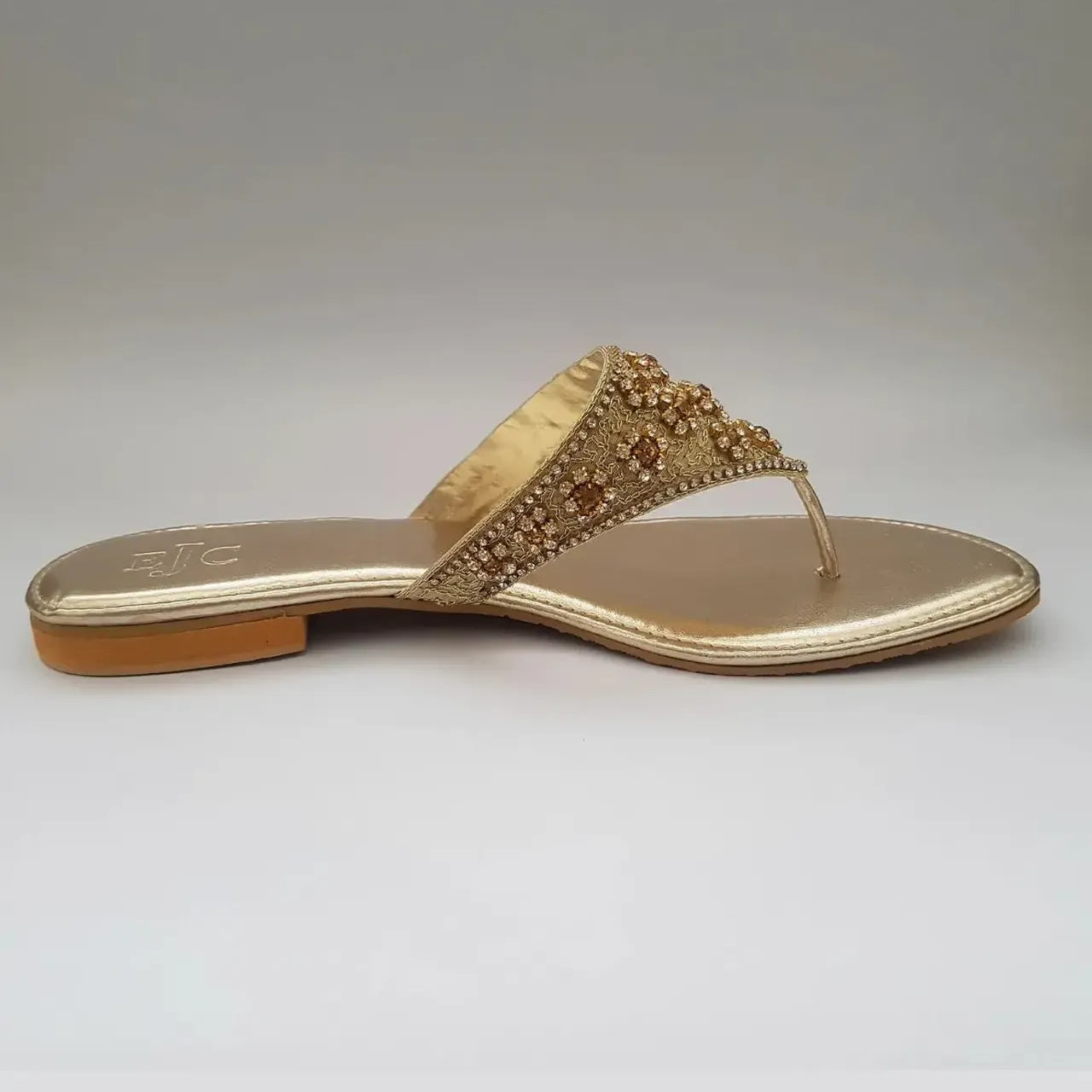 Gold sandal with embellishments on a light gray background