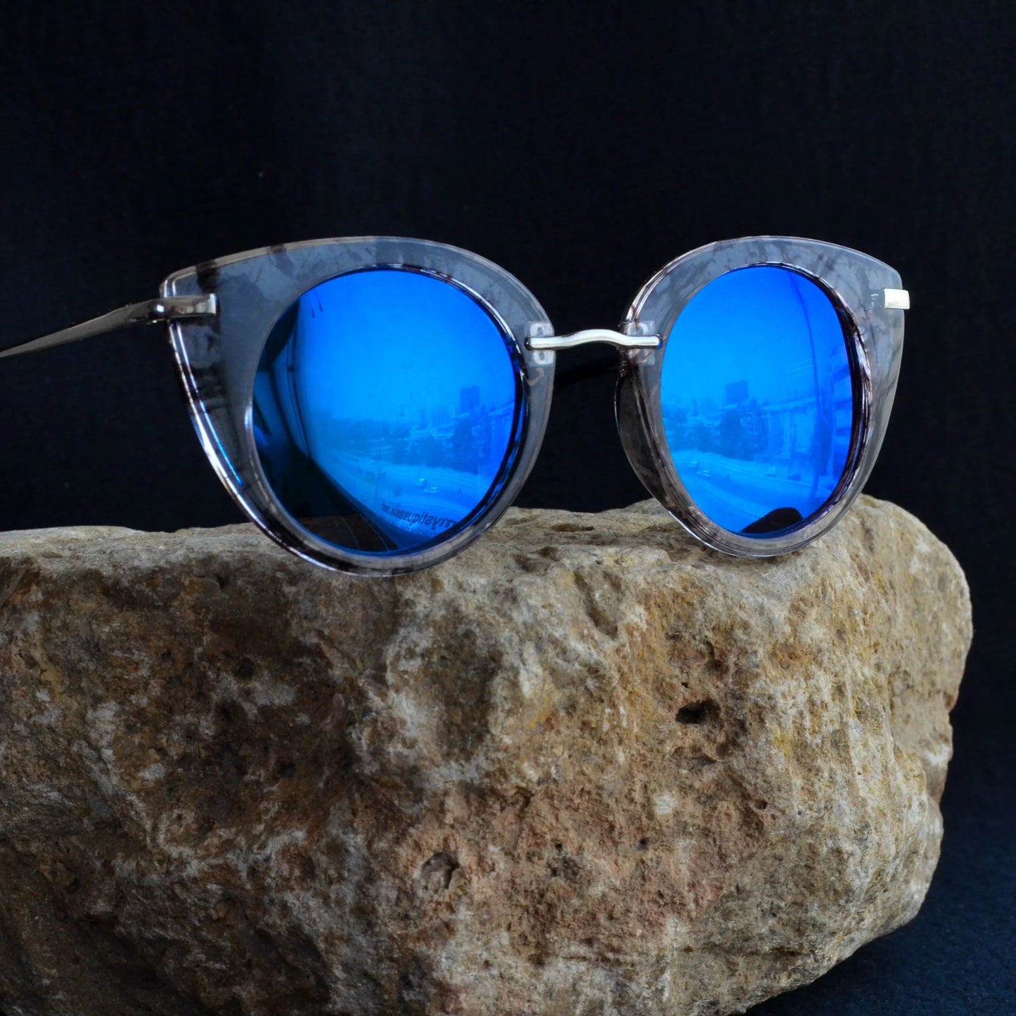 Sunglasses with blue lenses on a rock against a dark background