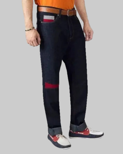 Person wearing dark blue jeans with a red patch on a plain background
