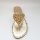 Gold sandal with embellishments on a light gray background