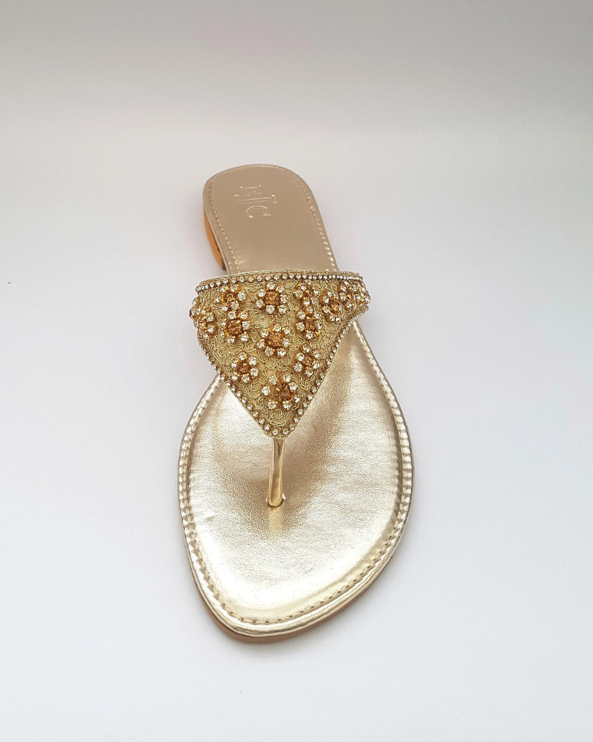 Gold sandal with embellishments on a light gray background
