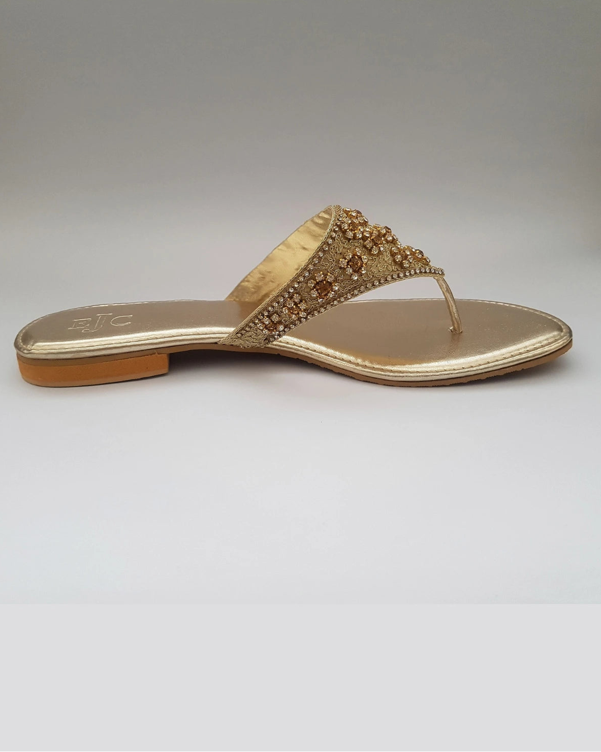 Gold sandal with embellishments on a light gray background