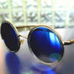 Round sunglasses with blue lenses and gold frames on a reflective surface.