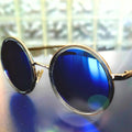 Round sunglasses with blue lenses and gold frames on a reflective surface.