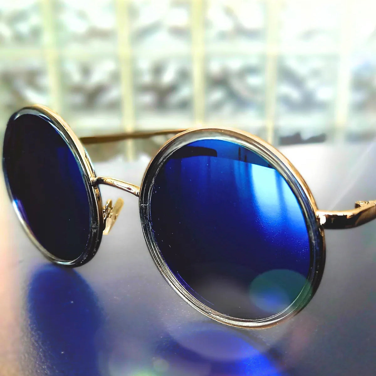 Round sunglasses with blue lenses and gold frames on a reflective surface.