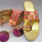 A pair of baby pink open-toed flat summer shoes with decorative embellishments, displayed alongside a pair of sunglasses.