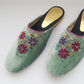 Pair of green slippers with floral embroidery on a white background