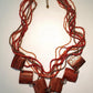 A multilayered handcrafted wooden necklace with red and brown beads and square wooden pendants, fastening with a clasp.