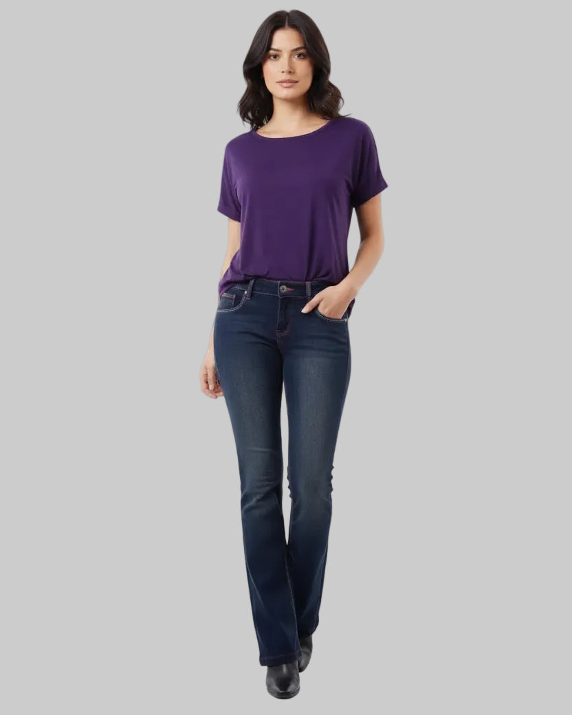 Woman wearing a purple shirt and dark blue jeans on a light gray background