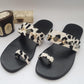 A pair of black velvet flip flops with white leopard print straps and decorative buckles, displayed alongside a wooden box possibly containing the packaging.
