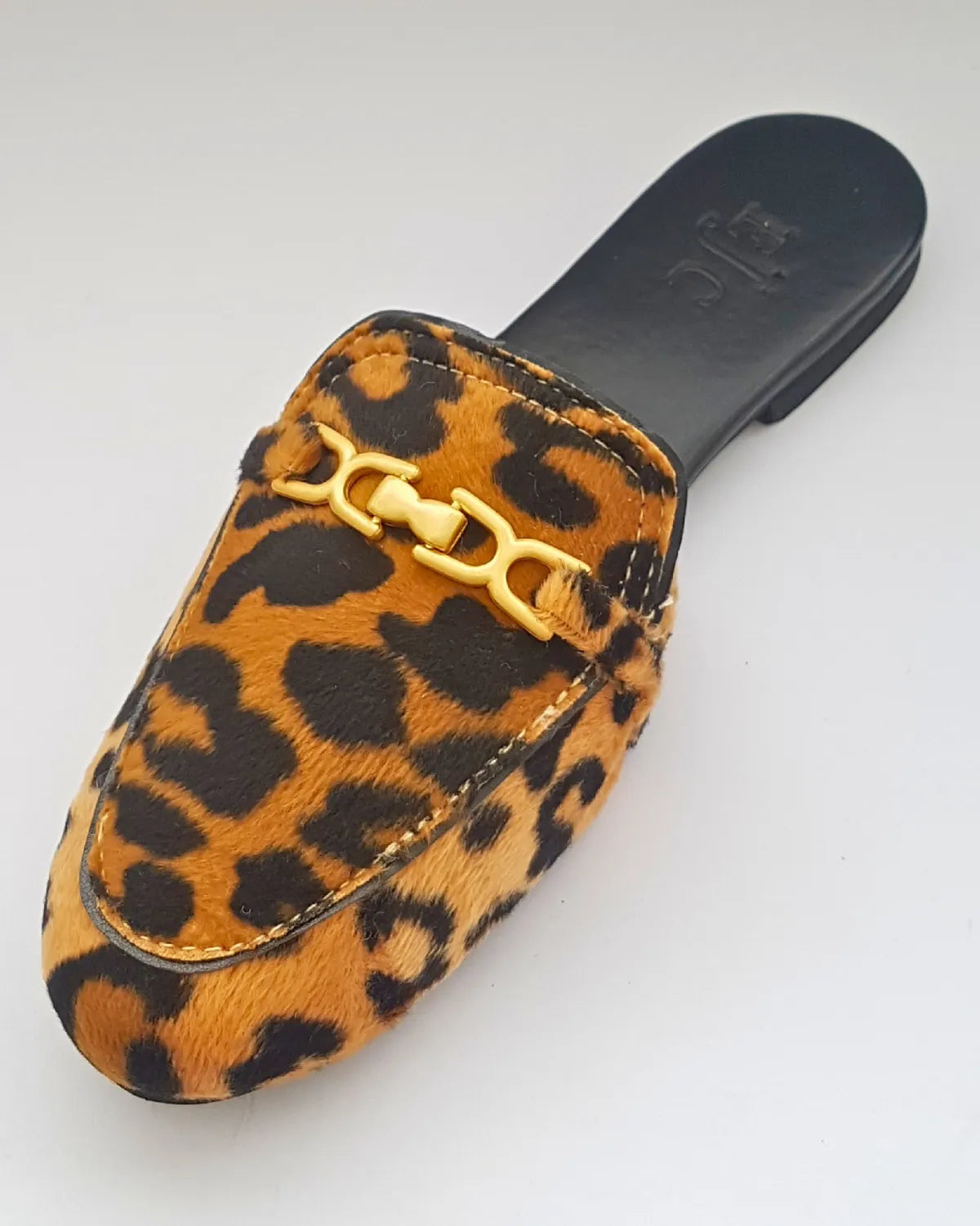 Leopard print slip-on shoe with a gold buckle on a white background