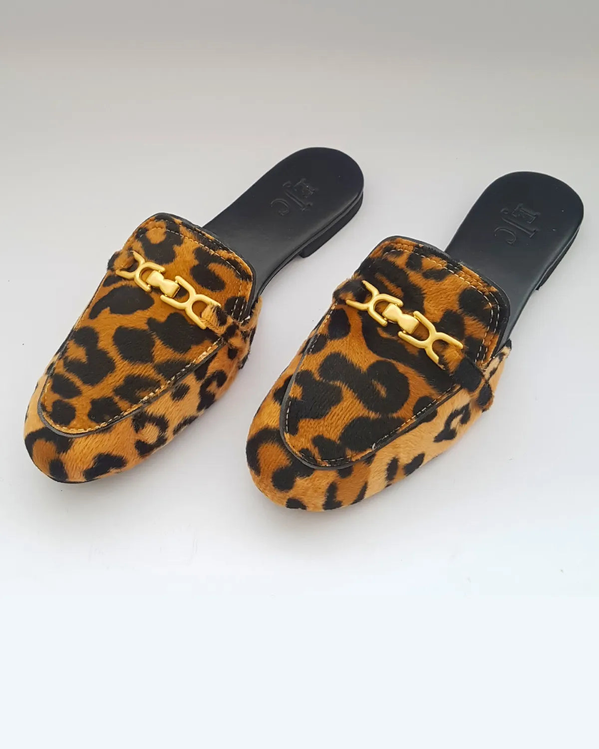 Pair of leopard print slippers with gold accents on a white background