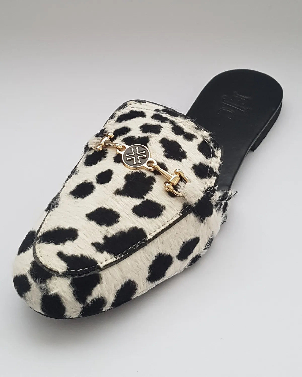 White slipper with black spots and gold logo on a white background