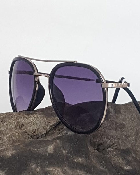 A pair of aviator-style sunglasses with black polarized lenses and metallic frame, displayed on a rock.