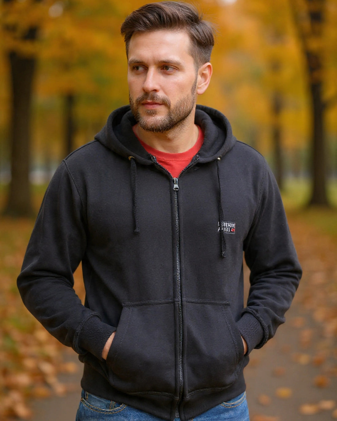 Man wearing a black hoodie with a logo in an autumn setting