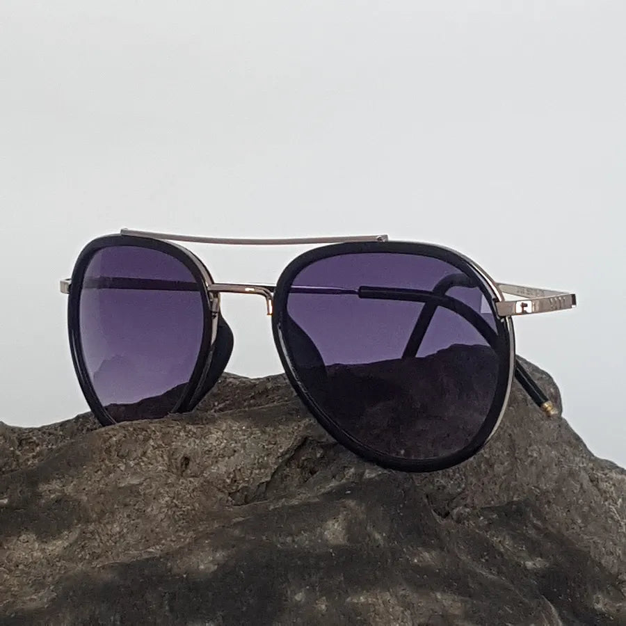 Sunglasses with purple lenses on a rock against a gray sky