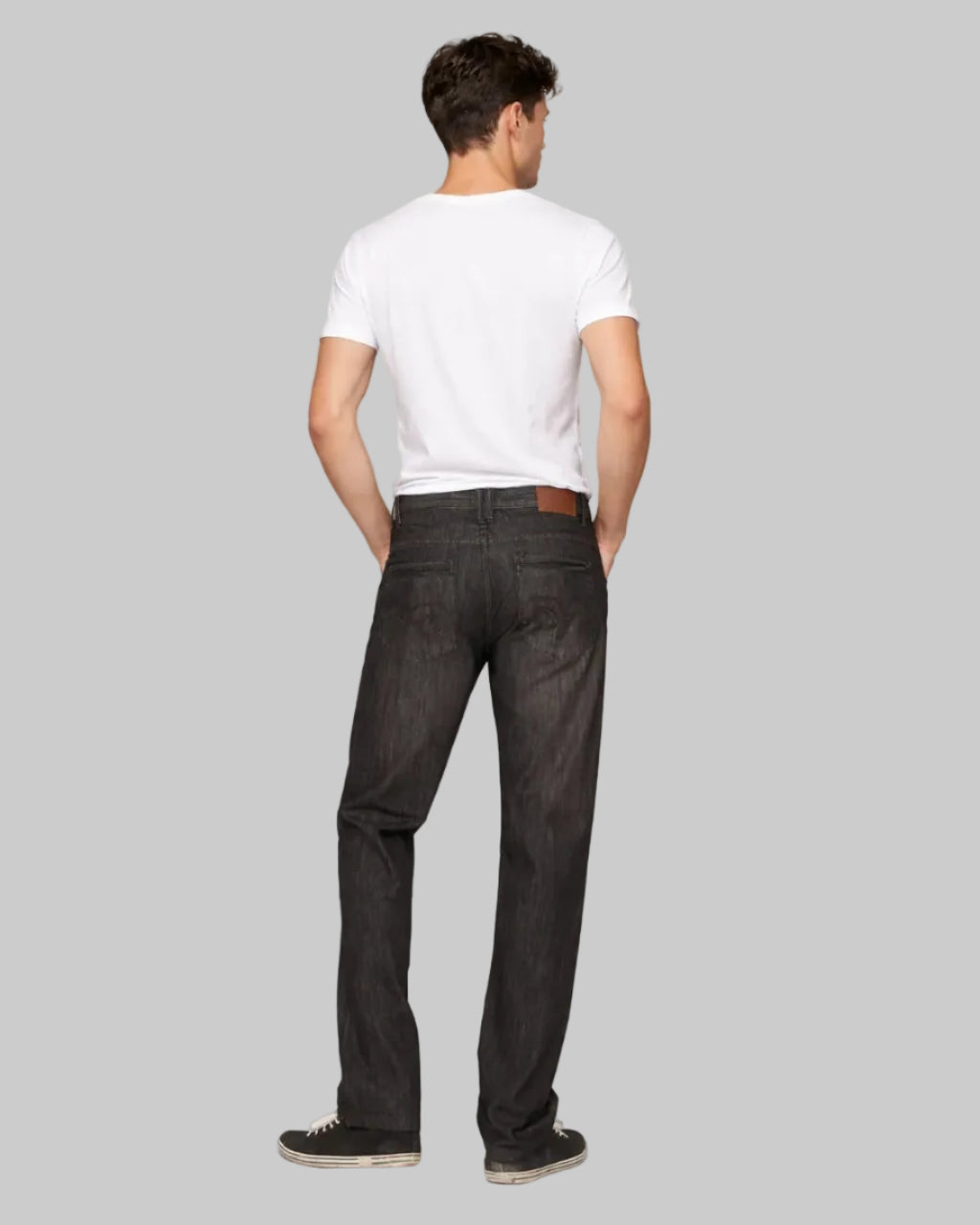 Man wearing a white t-shirt and black jeans on a gray background
