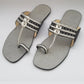 Pair of silver sandals with decorative straps on a light gray background