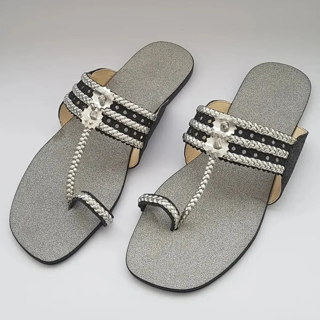 Pair of silver sandals with decorative straps on a light gray background