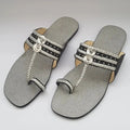 Pair of silver sandals with decorative straps on a light gray background