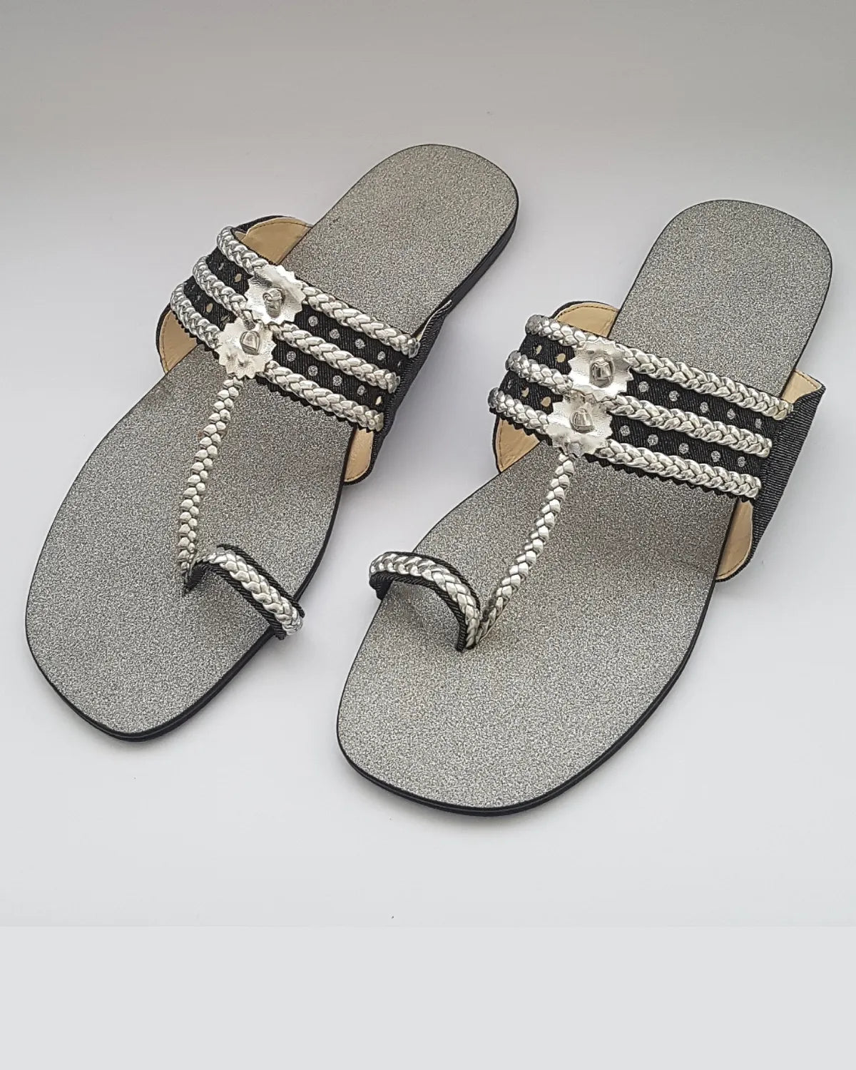Pair of silver sandals with decorative straps on a light gray background