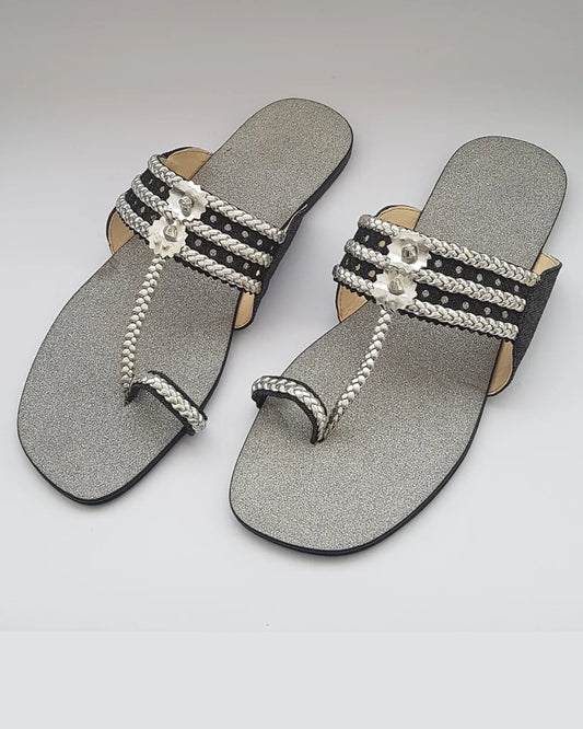 Pair of silver sandals with decorative straps on a light gray background