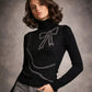 Woman wearing a black sweater with a bow design and gray pants against a gray background