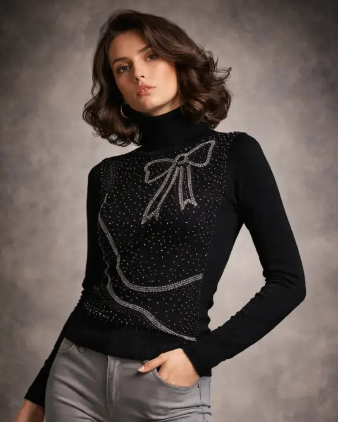 Woman wearing a black sweater with a bow design and gray pants against a gray background