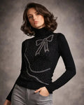 Woman wearing a black sweater with a bow design and gray pants against a gray background