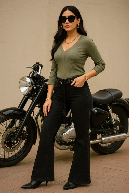 Woman in green top and black pants standing next to a motorcycle on a beige background