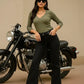Woman in green top and black pants posing with a motorcycle on a beige background
