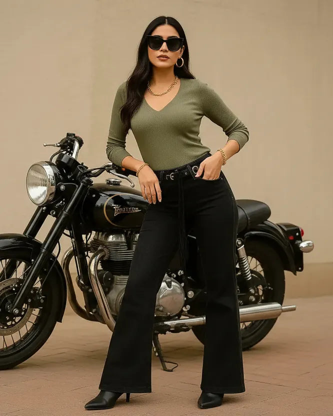 Woman in green top and black pants standing next to a motorcycle on a beige background
