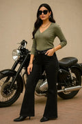 Woman in green top and black pants standing next to a motorcycle on a beige background