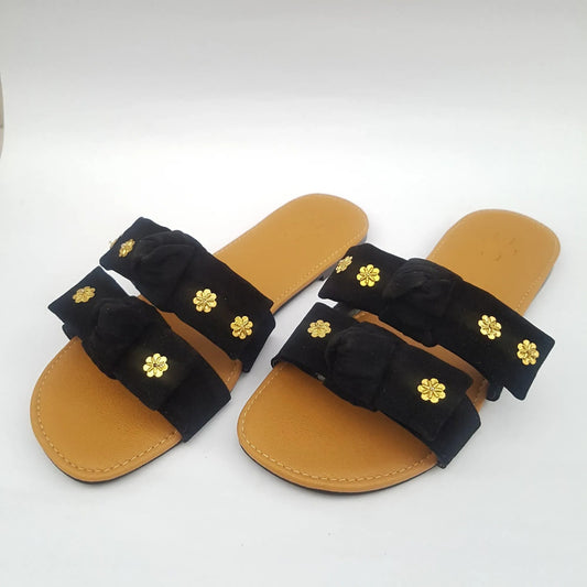 Pair of sandals with black straps and gold flower embellishments on a white background