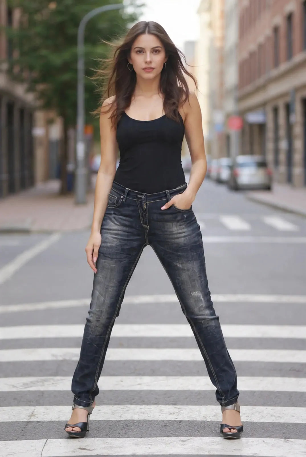 Woman in black tank top and jeans standing on a city street crosswalk.