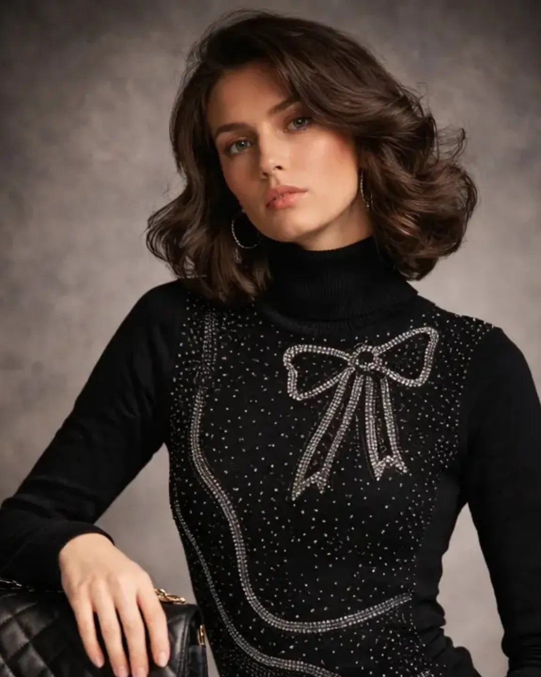 Woman wearing a black sweater with a bow design and gray pants against a gray background