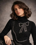 Woman wearing a black sweater with a bow design, holding a black handbag.