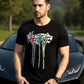 Man wearing a black t-shirt with colorful graphic design in front of a sports car.