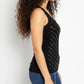 Woman wearing a black sleeveless top with white pattern and blue jeans against a white background