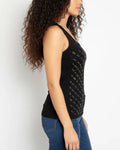 Woman wearing a black sleeveless top with white pattern and blue jeans against a white background