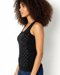 Woman wearing a black tank top with white patterns against a plain background