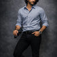 Man wearing a light blue shirt and black pants against a dark gray background