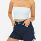Woman wearing a white strapless top and dark denim shorts on a plain background