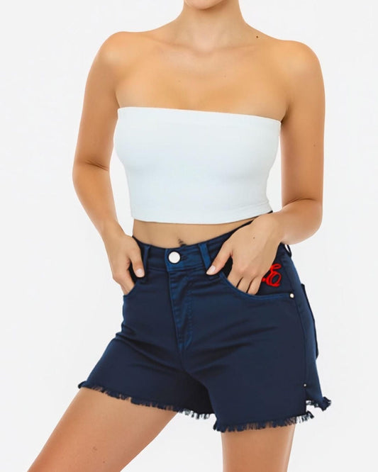 Woman wearing a white strapless top and dark denim shorts on a plain background