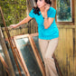 Woman in a blue shirt standing among broken glass panels outdoors